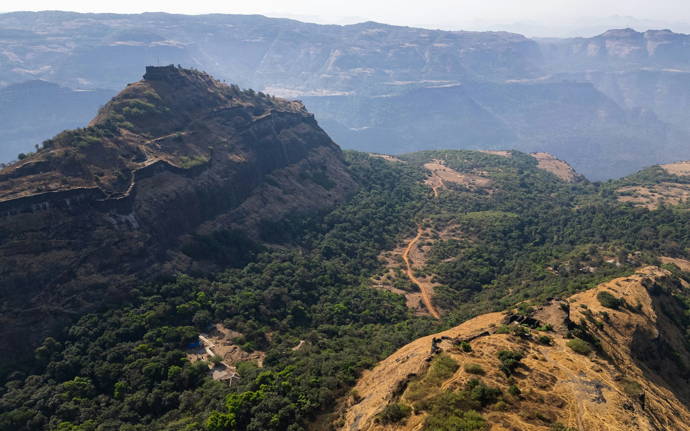 Forested Sahyadri hills and a dirt track below a hill fort, Maharashtra